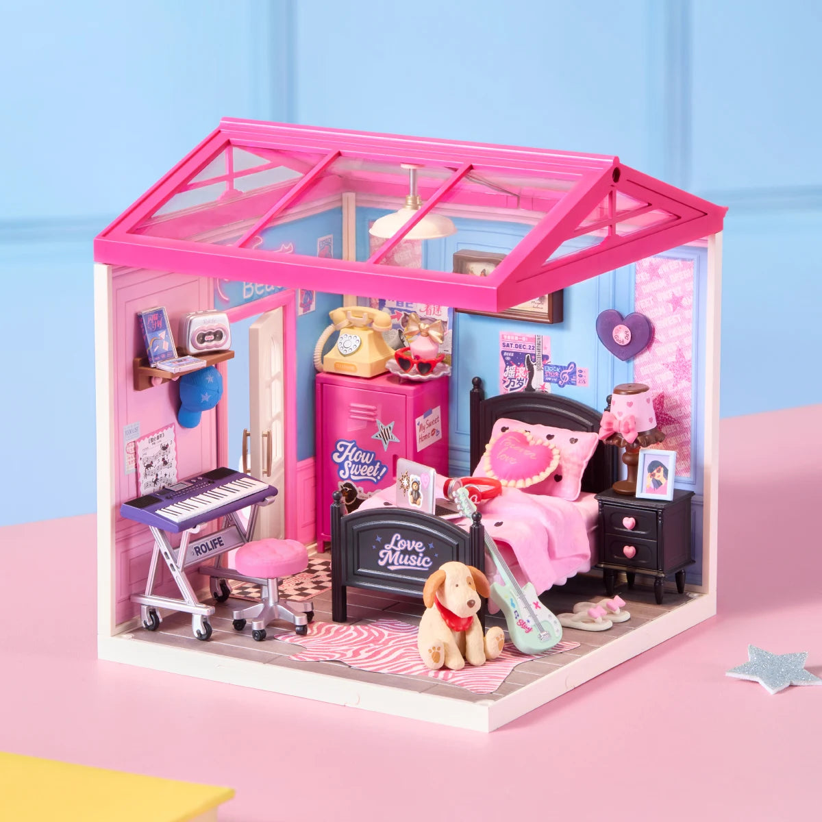 Rolife miniature bedroom diorama with pink roof frame, blue walls, black bed, pink bedding, keyboard, guitar, dog figure and music posters on a pink surface.