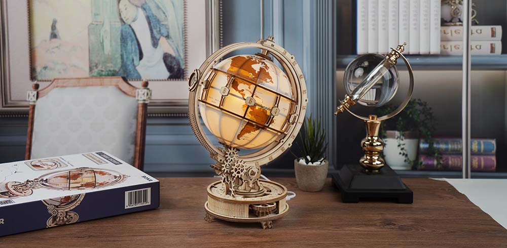 ROKR Luminous Globe 3D wooden puzzle displayed on a wide wooden desk in a study room with bookshelf, framed painting and crystal globe in background