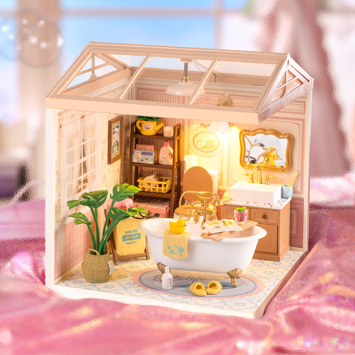Front-facing view of Rolife Pop Bubble Bathroom miniature with text overlay reading Enjoy a Bubble Moment, set against a soft pink background.