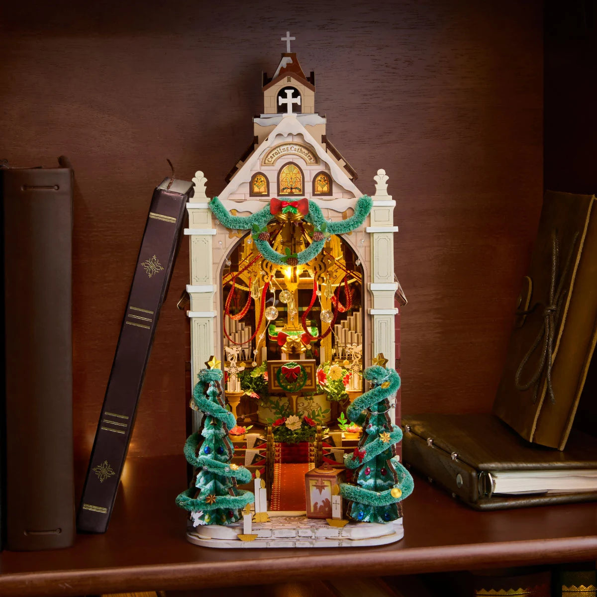 Rolife Weihnachts-Kathedralen-Miniatur in einem Holzregal zwischen stehenden Büchern, der Bogengang ist mit warmem Licht beleuchtet.