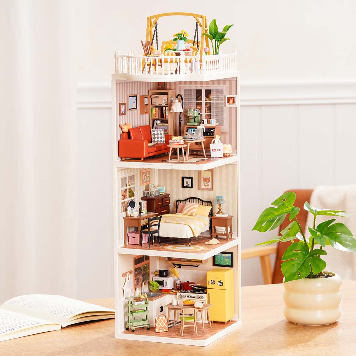 Rolife Super Creator Series 3-in-1 I Shape miniature tower with rooftop cafe terrace, pink bedroom, bathroom, and orange living room modules stacked beside a plant on a desk.