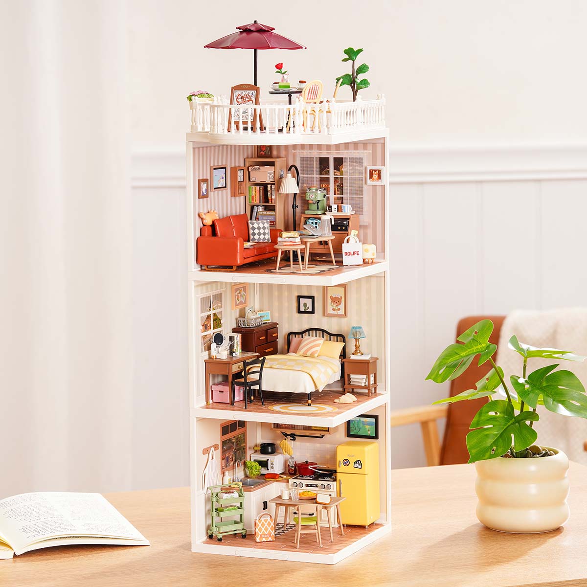 Rolife Super Creator Series 3-in-1 I Shape three-storey miniature tower with swing rooftop, bedroom, living room, and yellow kitchen modules in a white frame on a desk.
