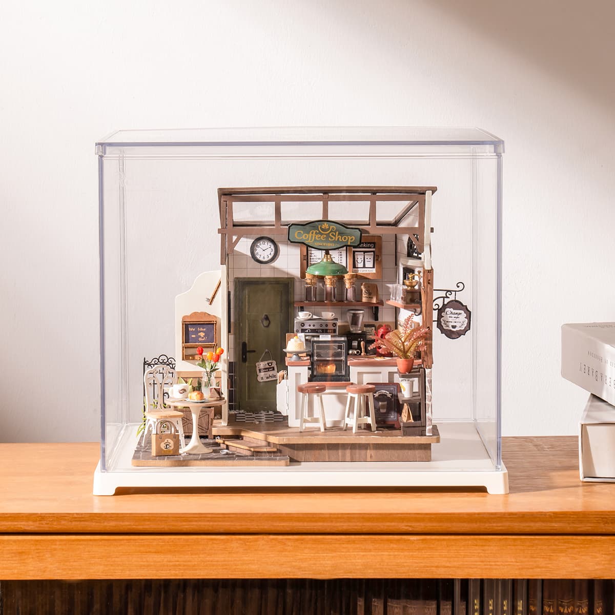Rolife cafe miniature sits inside a clear display box on a wooden tabletop.