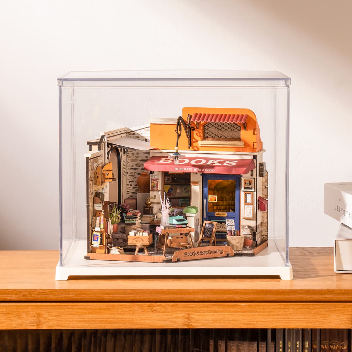 Rolife Corner Bookstore miniature sits under a clear case with an orange awning.