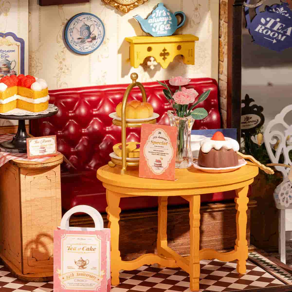 Rolife Leisure Time Tea Room DG171 miniature displayed on a wooden desk beside stacked books, with the blue Victorian storefront glowing warmly