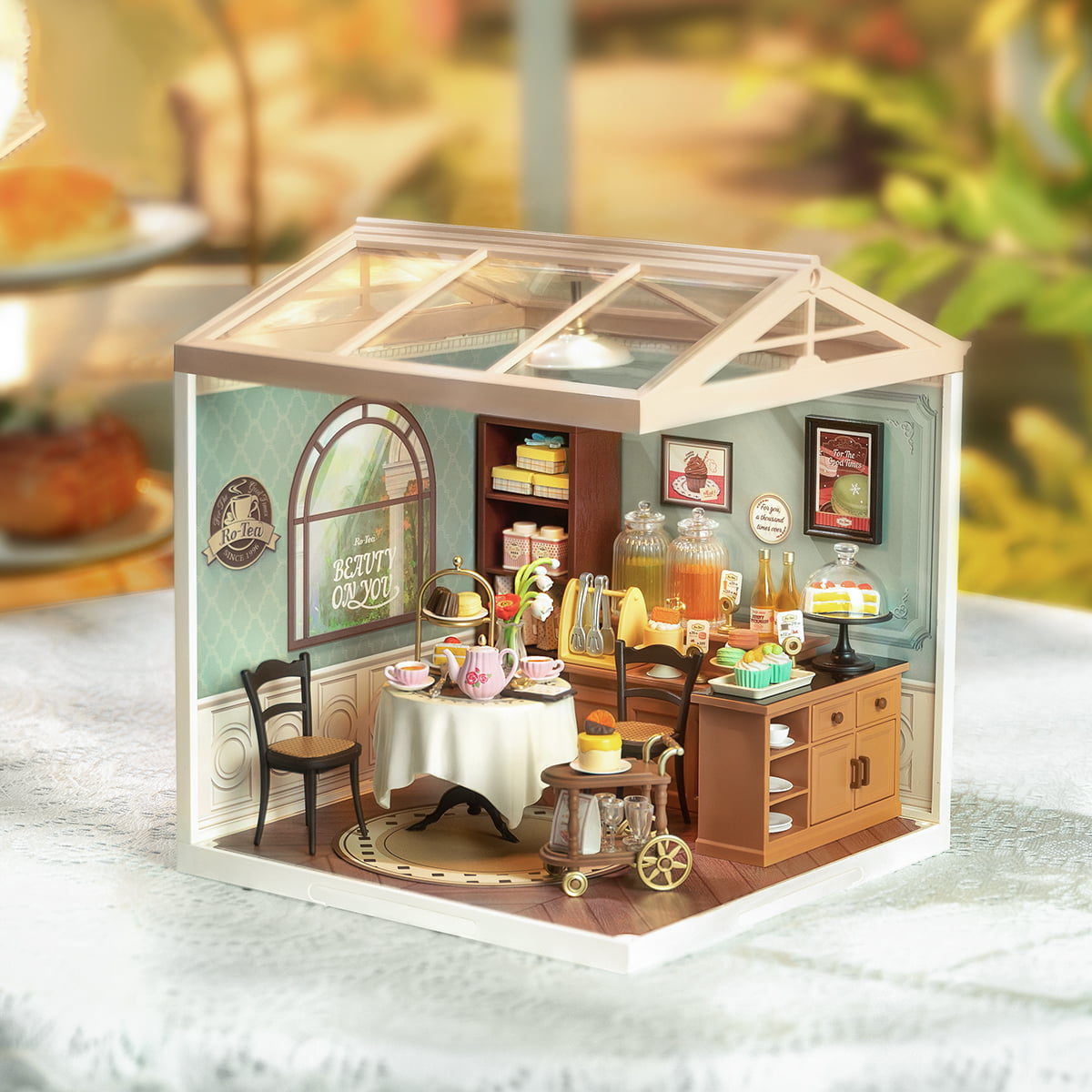 Rolife Sweet Sips Tea DW011 lit miniature tea salon in autumn garden setting with character figurine and warm amber interior lighting