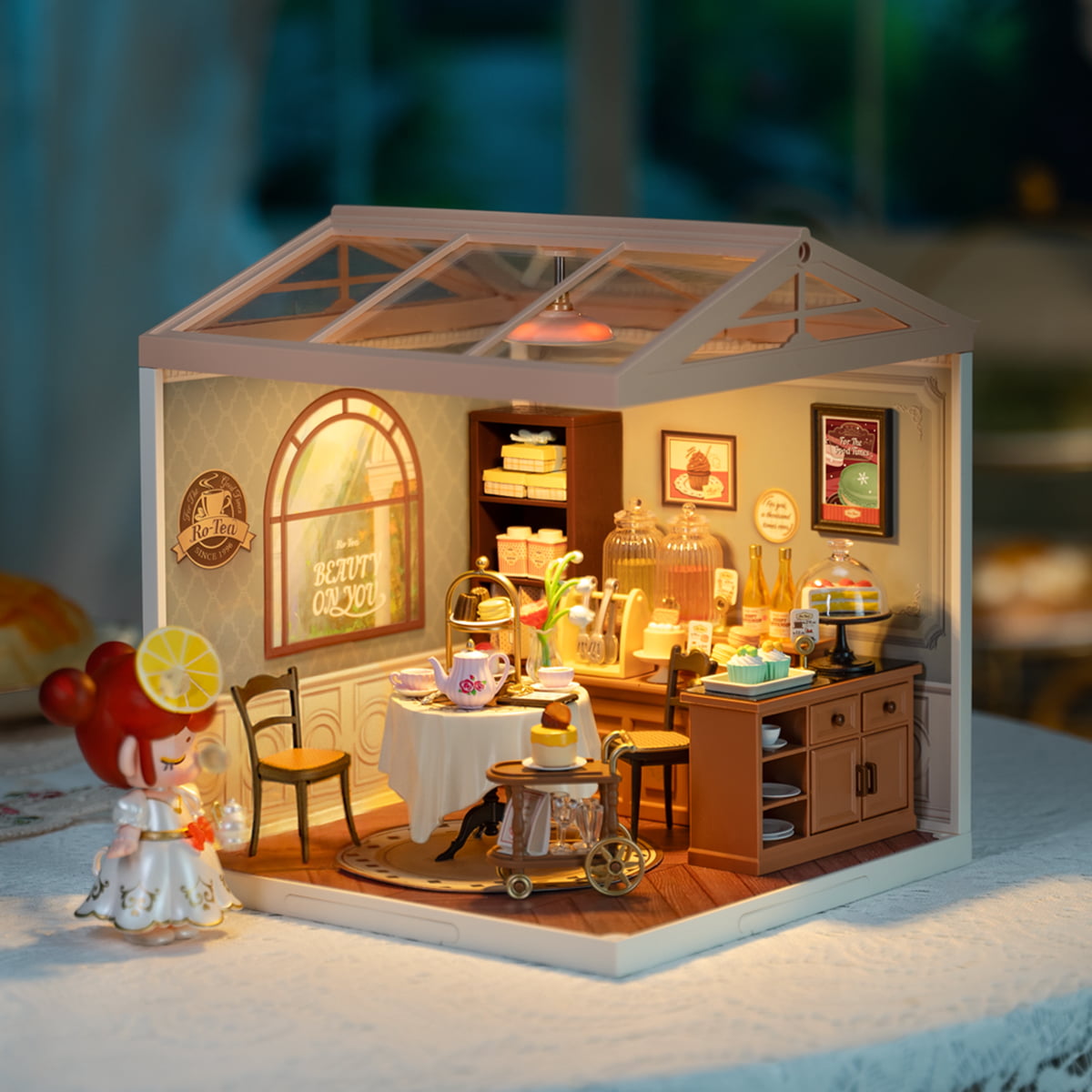 Rolife Sweet Sips Tea DW011 miniature tea room with greenhouse glass roof glowing with warm LED light shown beside a lemon and blossoms