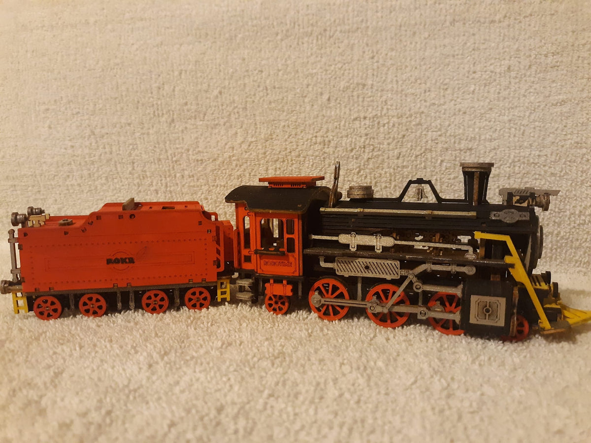 Fan-built ROKR painted locomotive model displayed on a fluffy white surface showing a black steam engine with red wheels and orange tender car