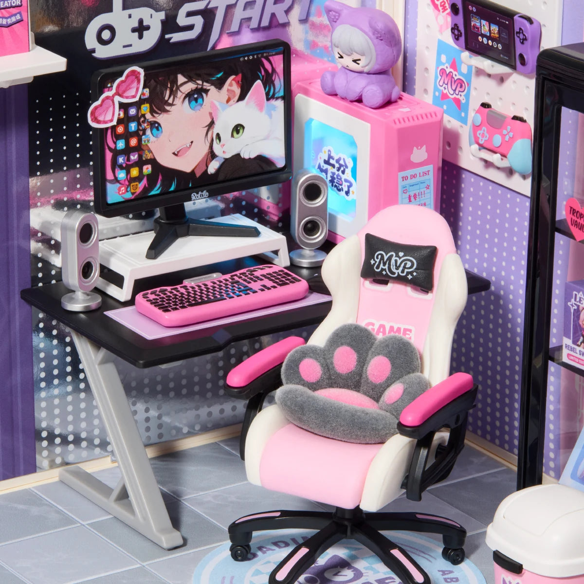 Close-up of miniature gaming desk with pink keyboard, monitor showing anime character, pink and white gaming chair with paw cushion, and speakers.