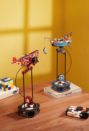 Robotime Gravity Swing collection theme graphic showing two ROKR pendulum balance airplane models on wooden desk