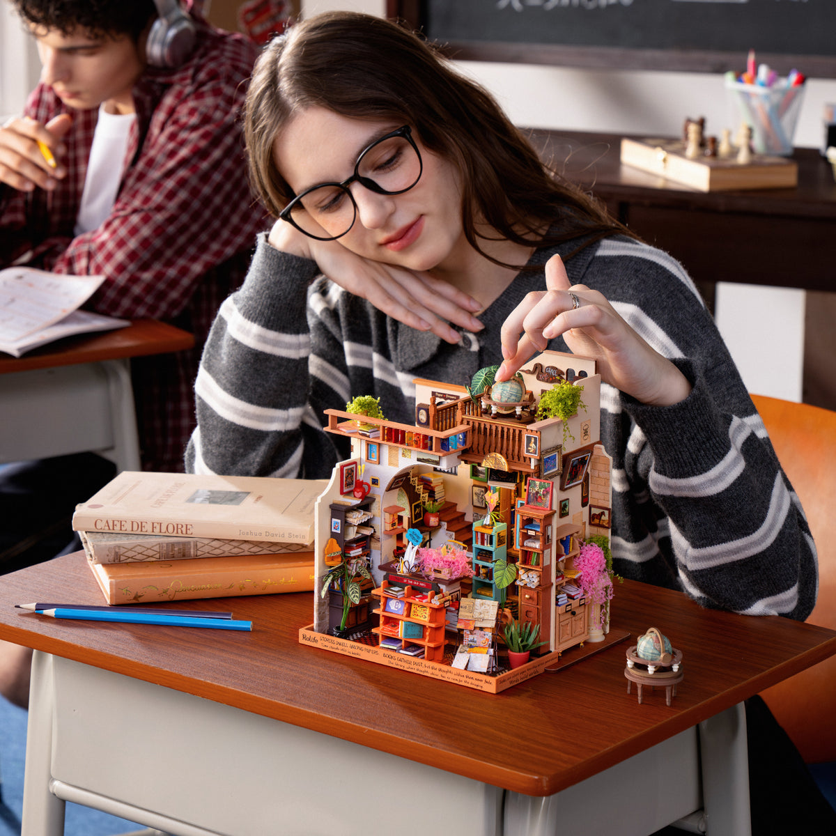 Woman placing a tiny rooftop detail on the PageStory Books miniature at her school desk