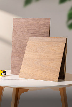 Two natural wood plywood sheets of different sizes leaning against each other on a white round table with green plant nearby