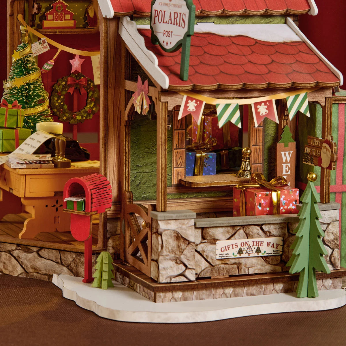 Close-up of the Rolife miniature post office porch with red mailbox, Polaris Post sign, stone-textured base, green trees and Gifts on the Way sign.
