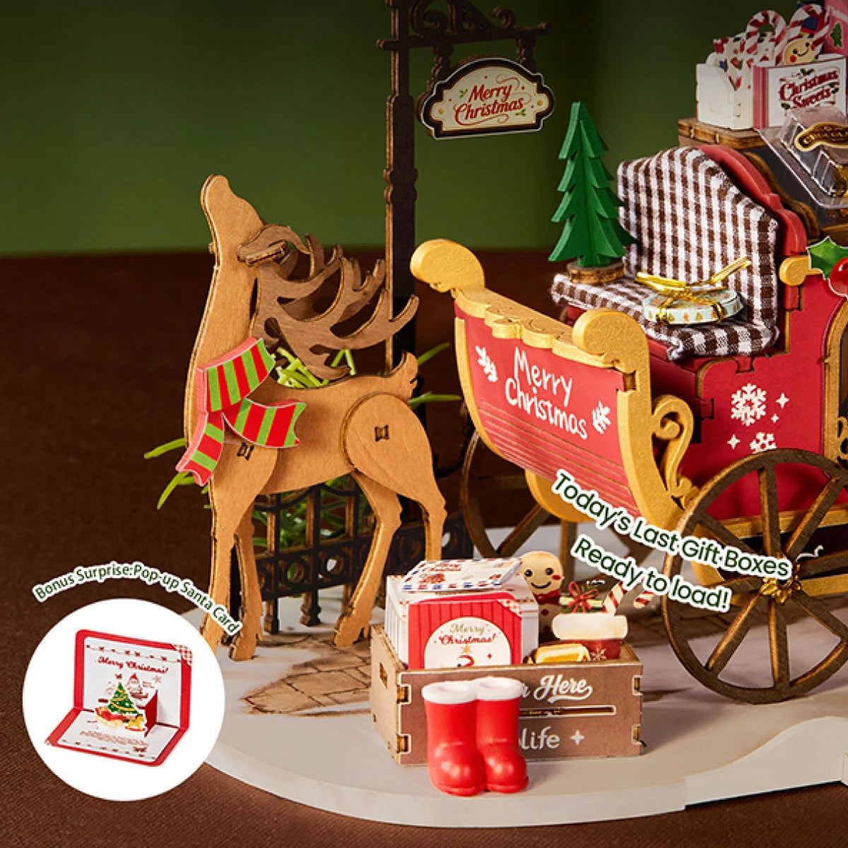 Close-up of a wooden reindeer with a red and green scarf beside a red sleigh, a crate of gifts, red boots, and a pop-up Santa card inset.