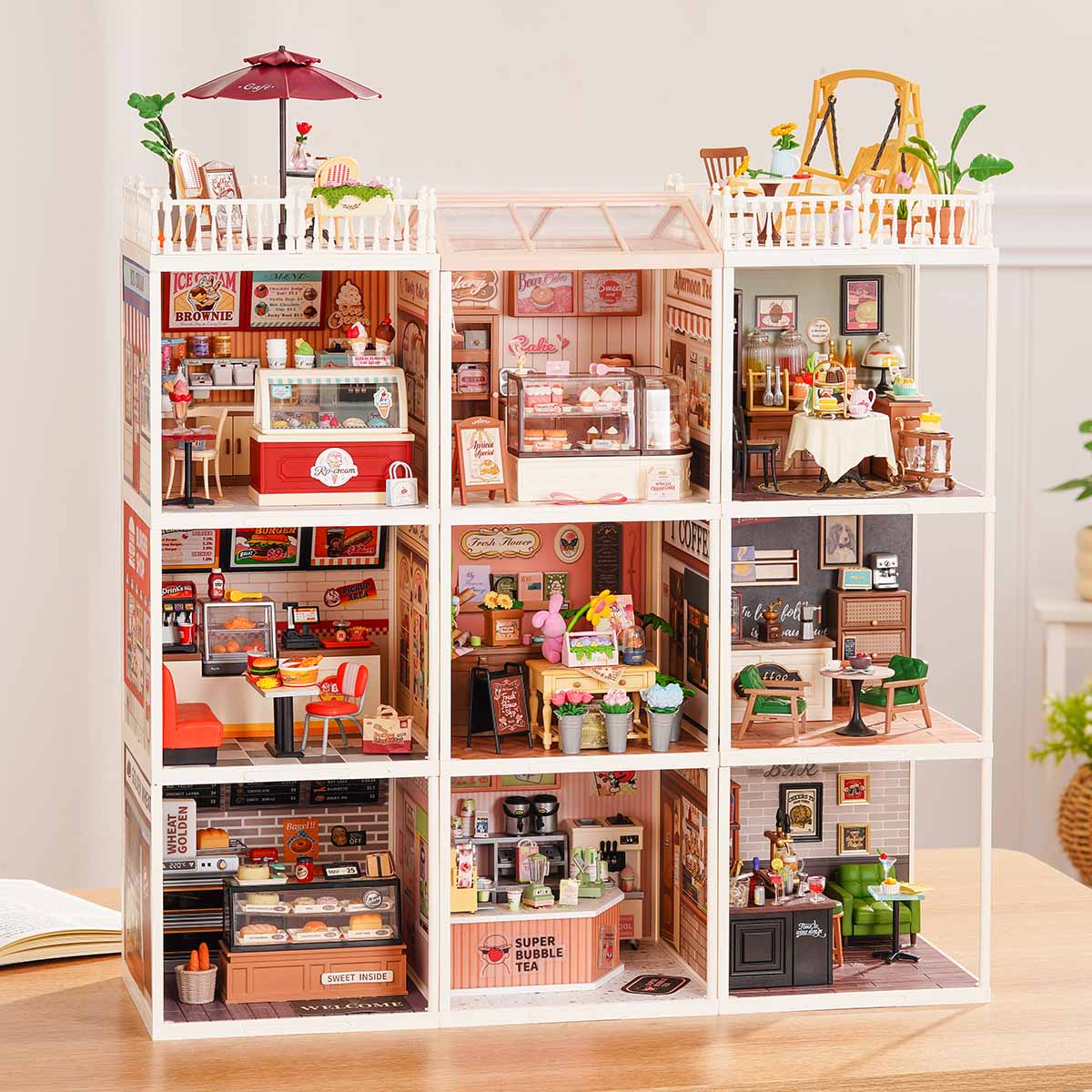 Rolife Super Creator Series 9-in-1 Nine Grid miniature building combining pink home rooms and colorful town shops under a white glass roof on a wooden table.