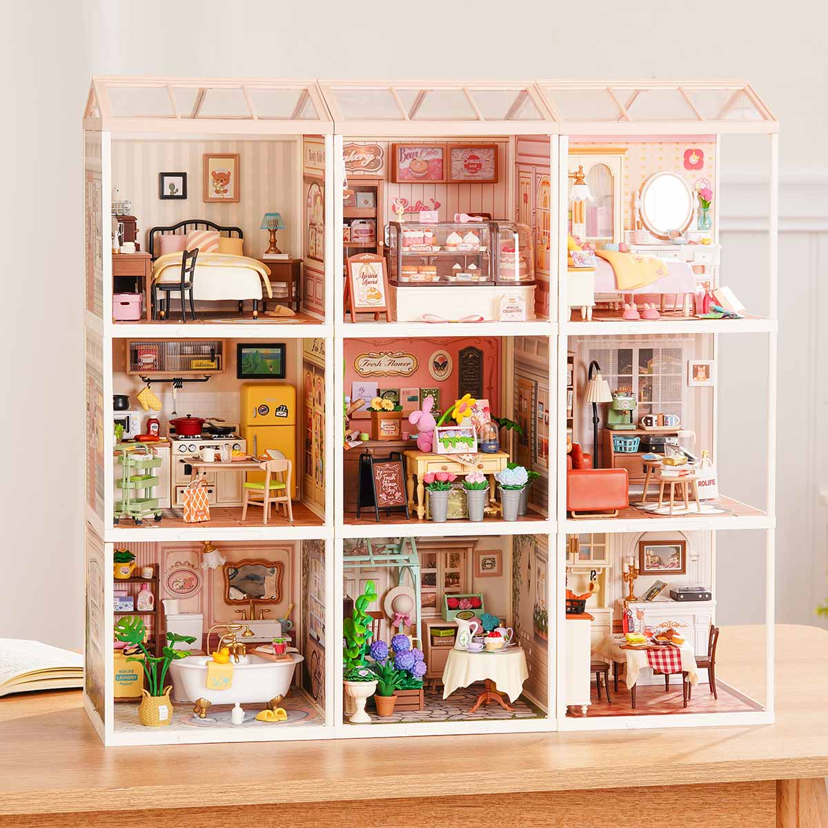 Rolife Super Creator Series 9-in-1 Nine Grid modular dollhouse with pink home rooms including bedroom, bakery, bathroom, and garden terrace on a wooden desk.