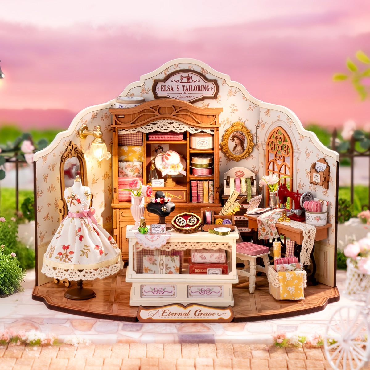 Rolife Elsa's Tailoring DG178 full miniature shop at dusk showing pink sky background, dress mannequin, wardrobe, counter and sewing area all assembled