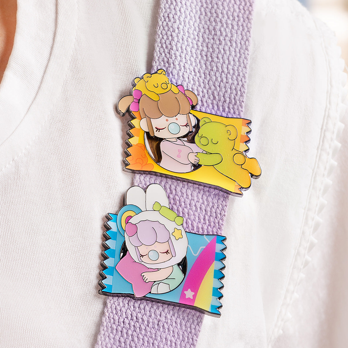 Two Rolife Nanci Sweet Time candy-wrapper enamel pins pinned to a white knit fabric showing the Hug bear design in yellow-orange and the Fluffy Cloud design in blue