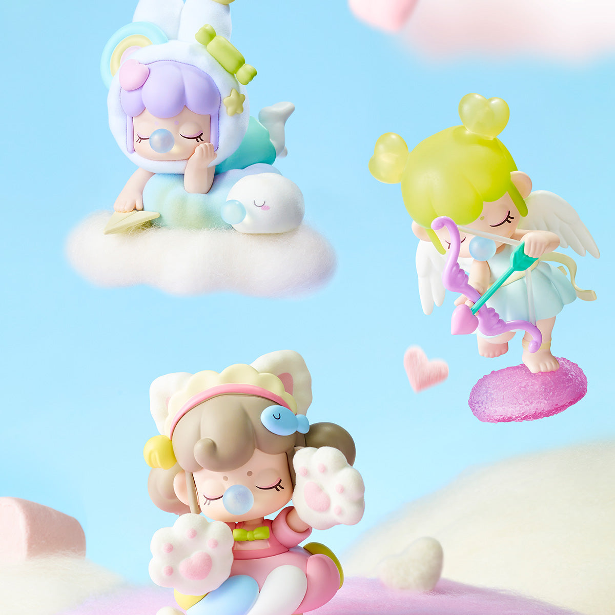 Three Rolife Nanci Sweet Time figures set against a blue sky showing a bunny on clouds, a translucent cupid angel, and a bear-costume figure in a candy landscape