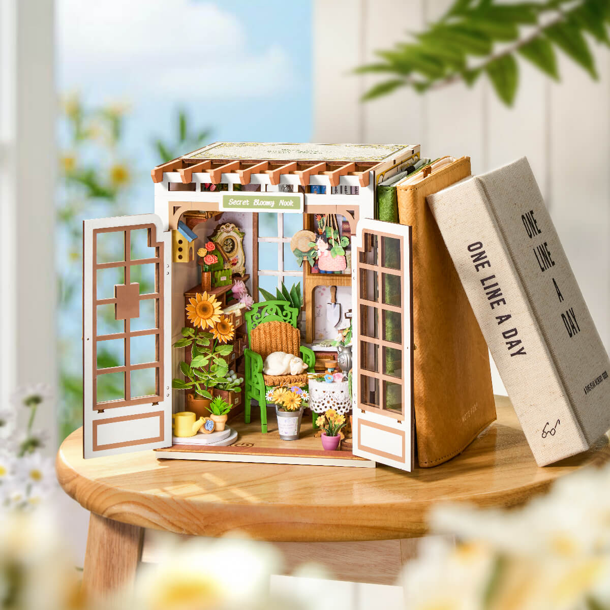 Rolife Secret Bloomy Nook placed between two books on a wooden surface, with white flowers in a soft blurred background