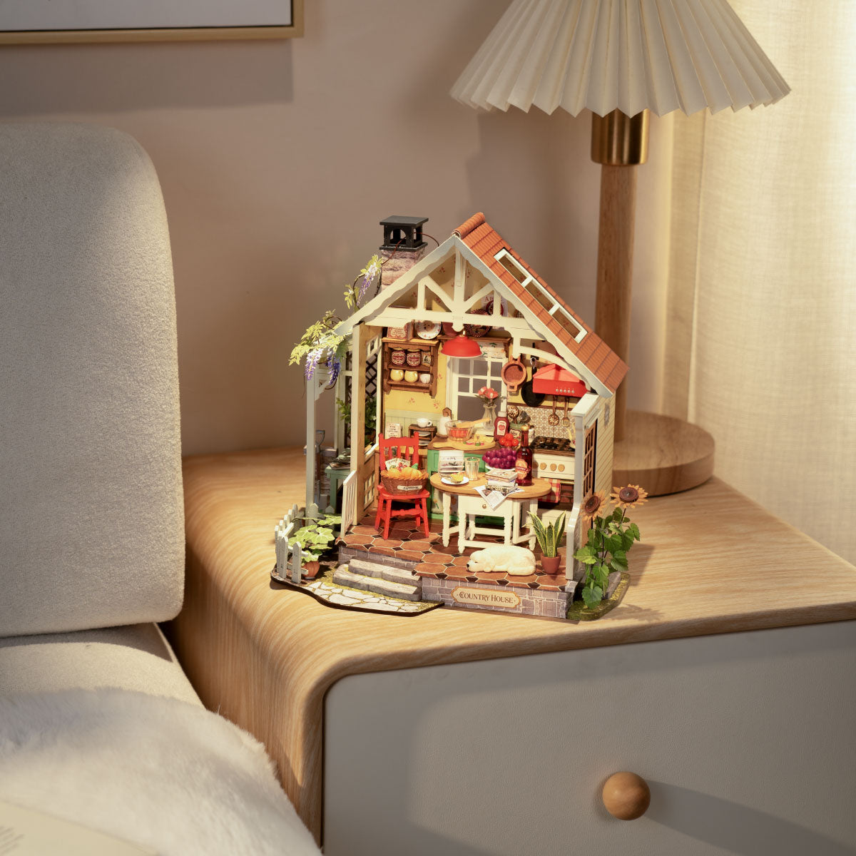 Rolife miniature farmhouse dollhouse placed on a bedside table beside a glowing lamp in a softly lit bedroom