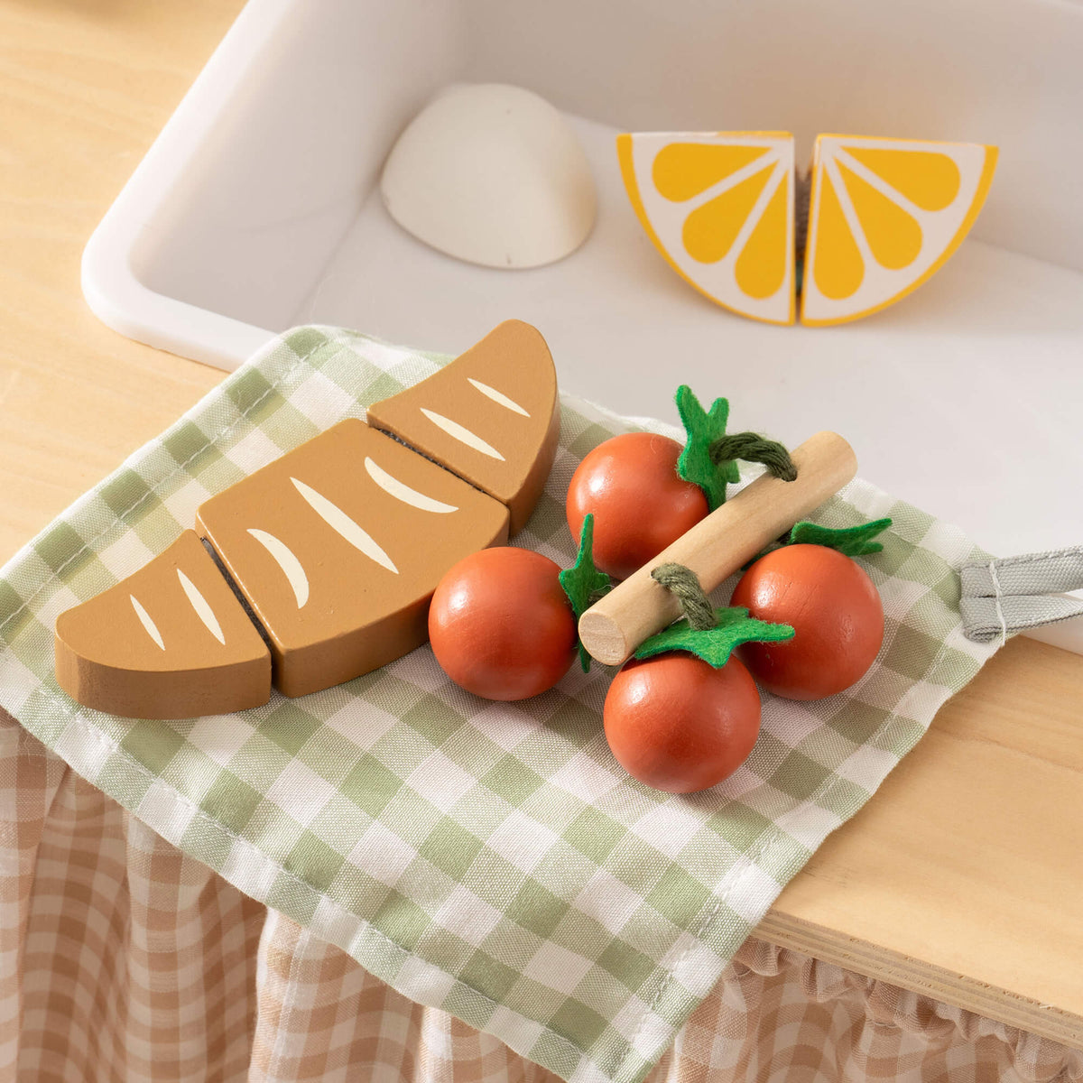 ROBUD wooden toy kitchen food accessories on a checkered cloth napkin including sliced bread, red cherry tomatoes and lemon halves