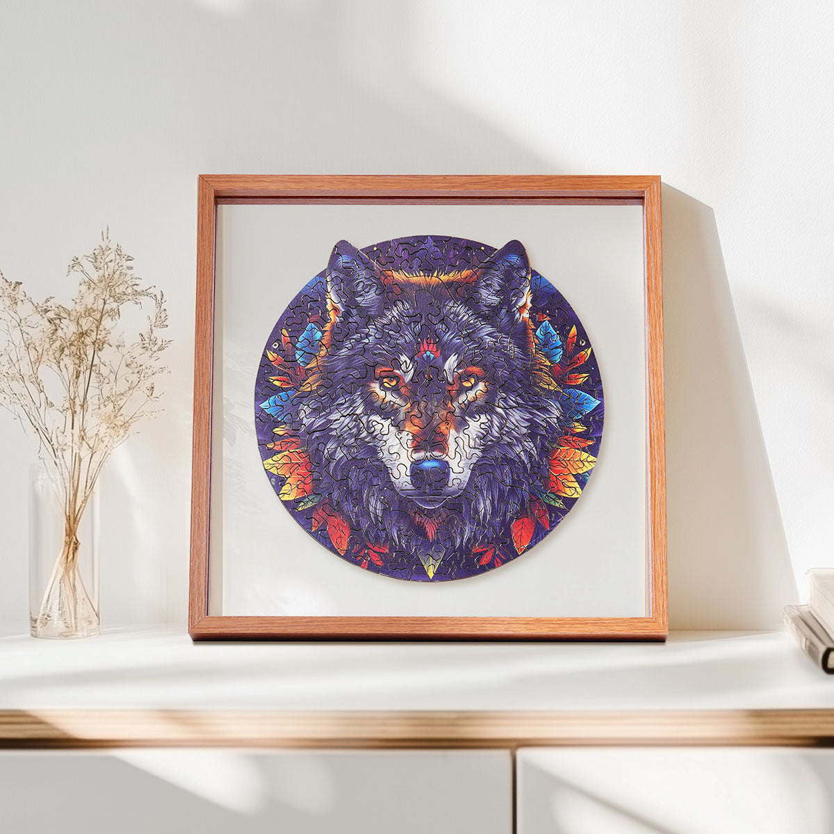 Rowood wolf head wooden jigsaw puzzle in a circular composition with colorful feather details, displayed in a warm wooden shadow box frame on a shelf