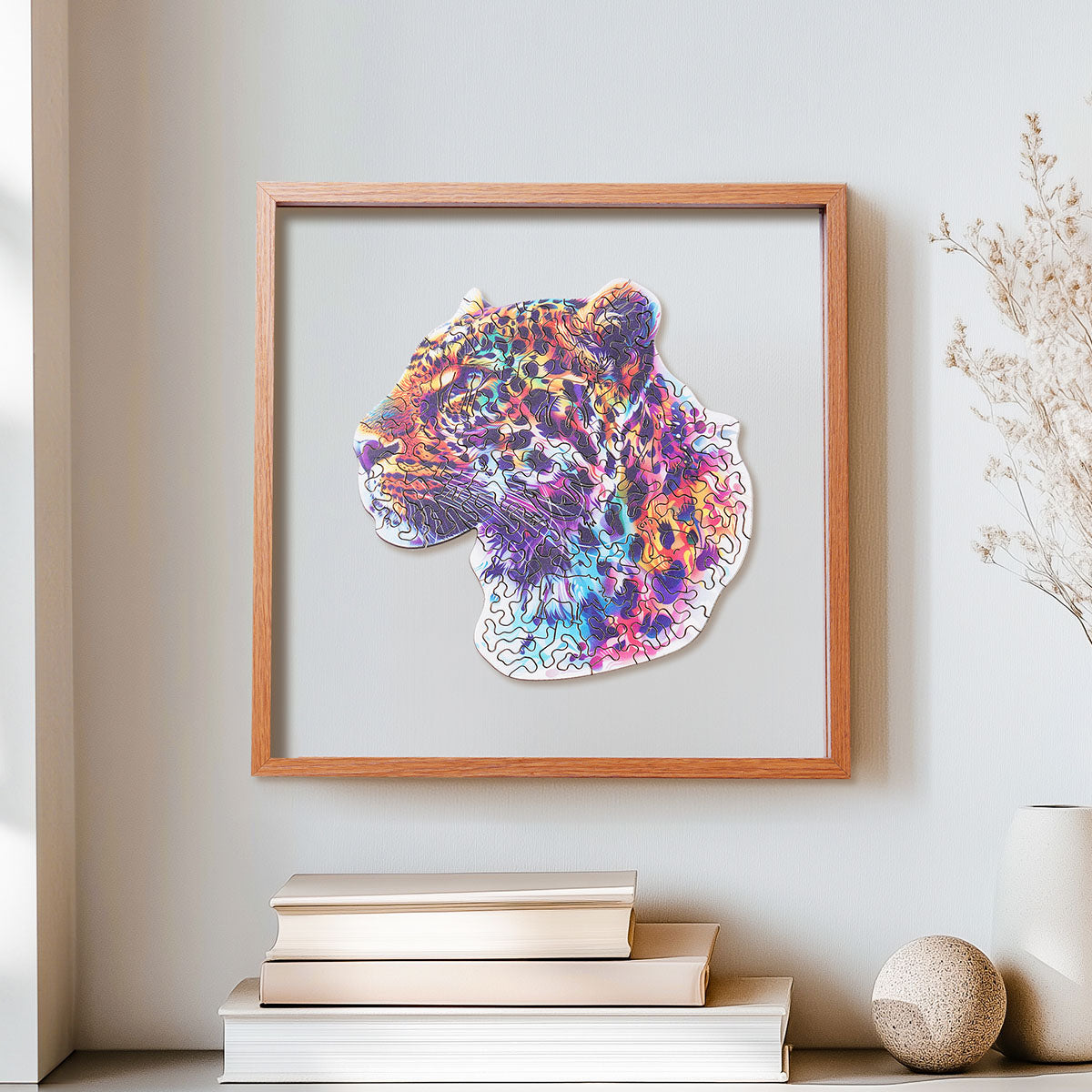 Rowood Fancy Leopard colorful wooden jigsaw puzzle in a shadow box frame hung on a wall above stacked books and a round stone ornament