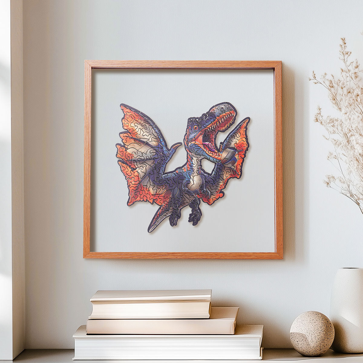 Rowood Fierce Pterosaur flying dinosaur wooden jigsaw puzzle in a shadow box frame hung on a wall above stacked books and a round stone ornament