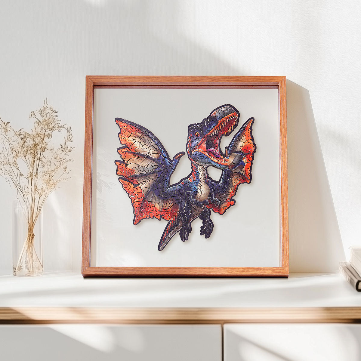 Rowood Fierce Pterosaur flying dinosaur wooden jigsaw puzzle in a shadow box frame resting on a shelf beside dried flowers and a small ceramic vase