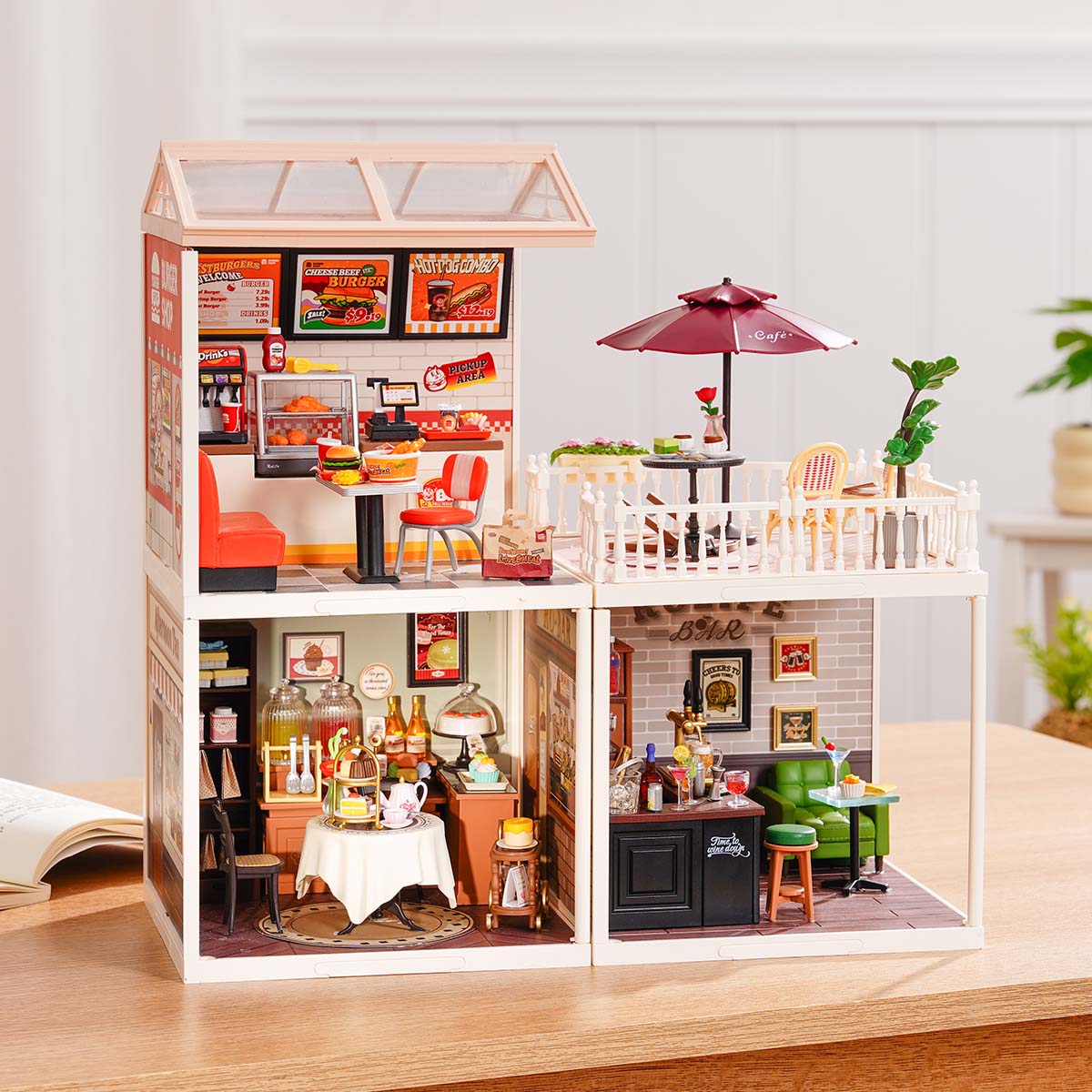 Rolife Super Creator Series 3-in-1 L Shape miniature with a burger restaurant on top and side cafe terrace beside lower afternoon tea and Rolife Bar modules on a wooden desk.