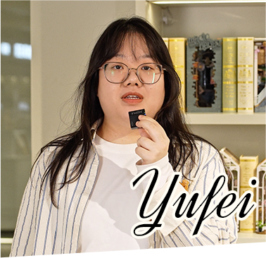 A Rolife team member named Yufei wearing glasses poses while speaking in front of bookshelves filled with Rolife miniature kits and decorative items