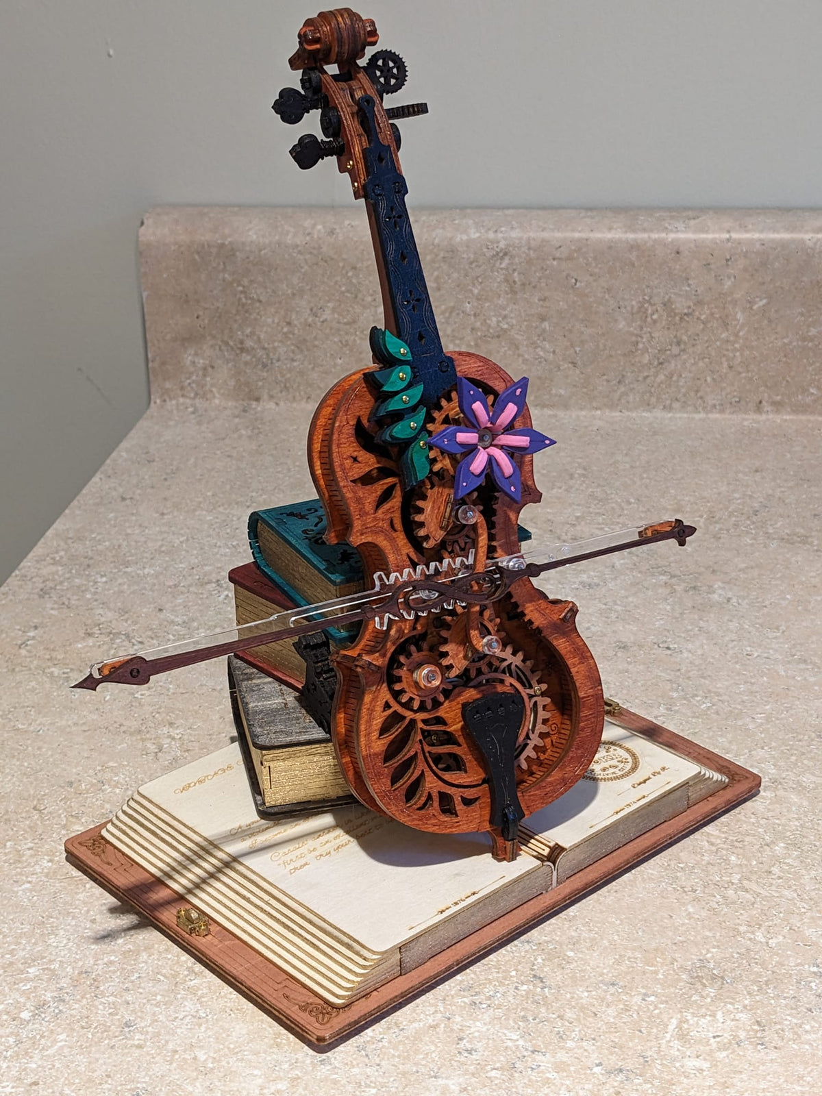Robotime violin music box sits on a base with crossed bow pieces and floral accents.