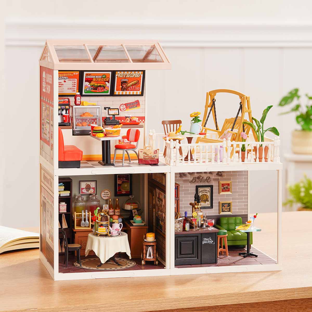 Rolife Super Creator Series 3-in-1 L Shape miniature in a horizontal layout showing six rooms including bedroom, flower garden cafe, kitchen, living room, dining room, and bathroom on a wooden surface.