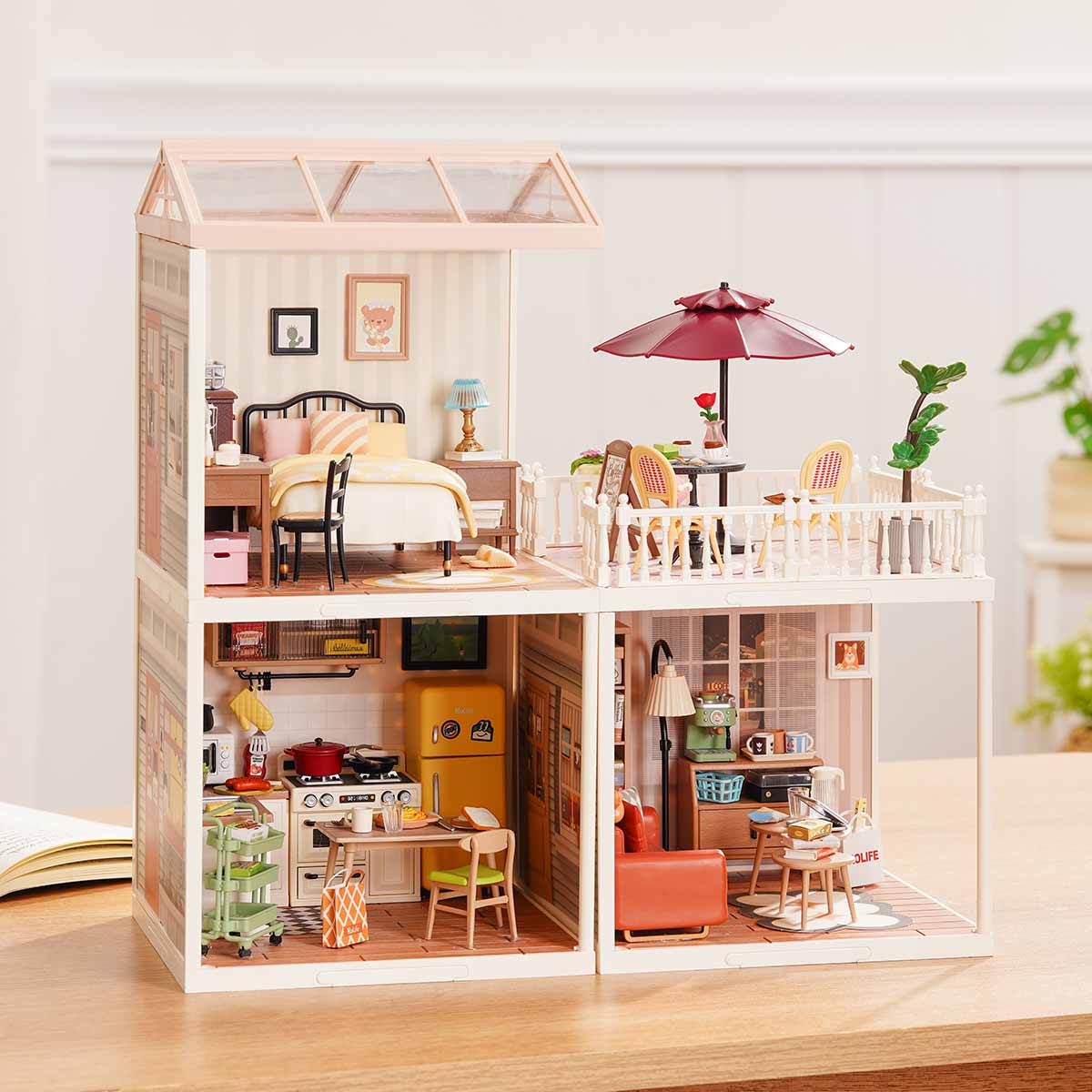 Rolife Super Creator Series 3-in-1 L Shape miniature in an L layout showing bedroom on top with rooftop umbrella terrace and lower kitchen plus living room beside a plant on a table.