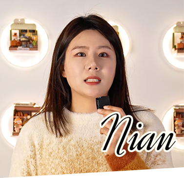 A Rolife team member named Nian poses in a cream sweater in front of circular wall sconces and Rolife miniature house displays in a retail setting