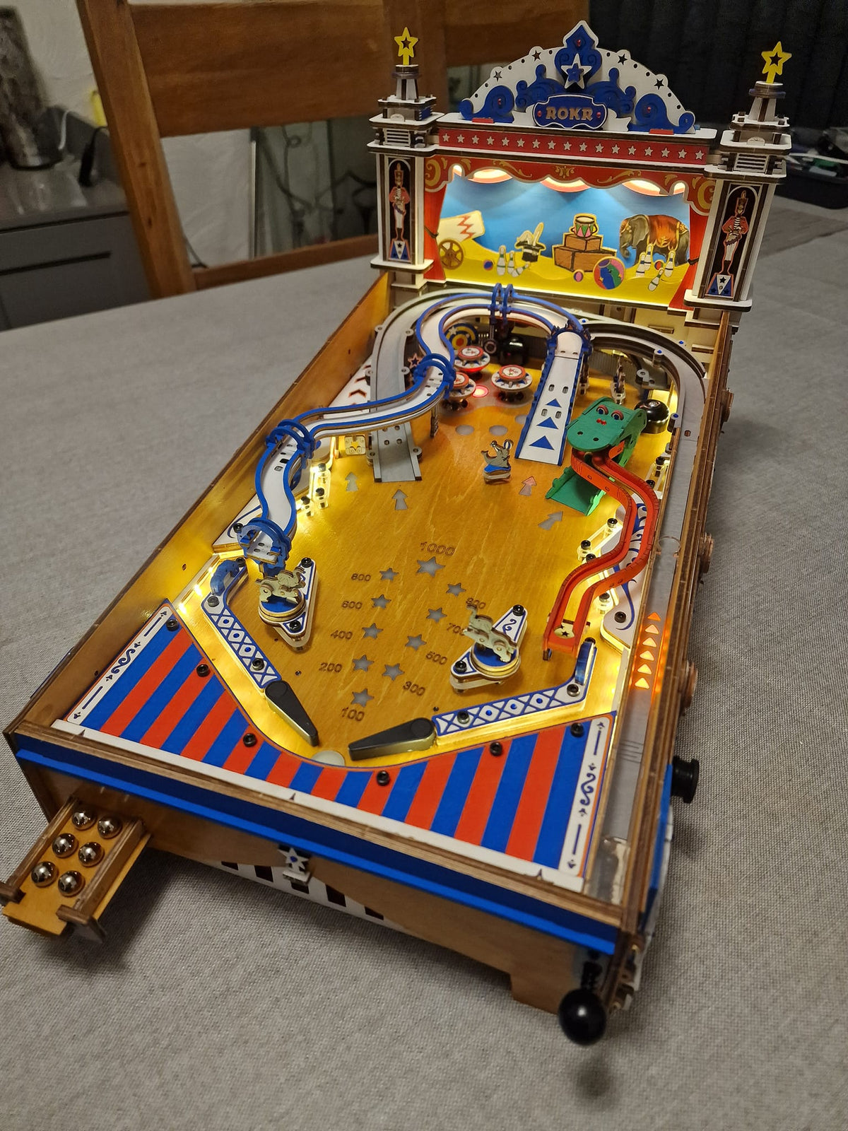 Robotime circus pinball table has blue ramps and a yellow playfield on a wooden table.