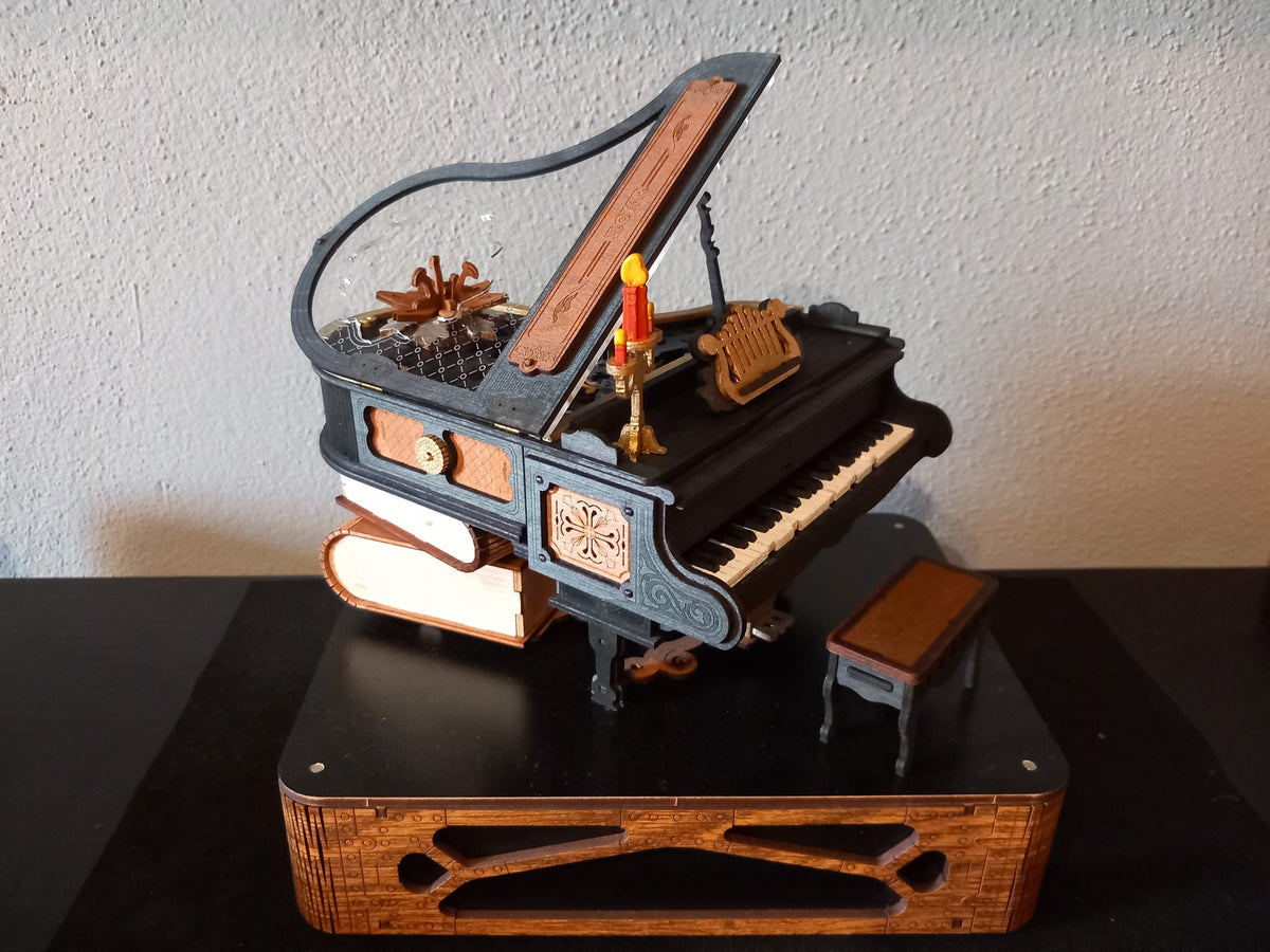 Wooden gramophone music box with a lit base and small brass horn on a dark tabletop.