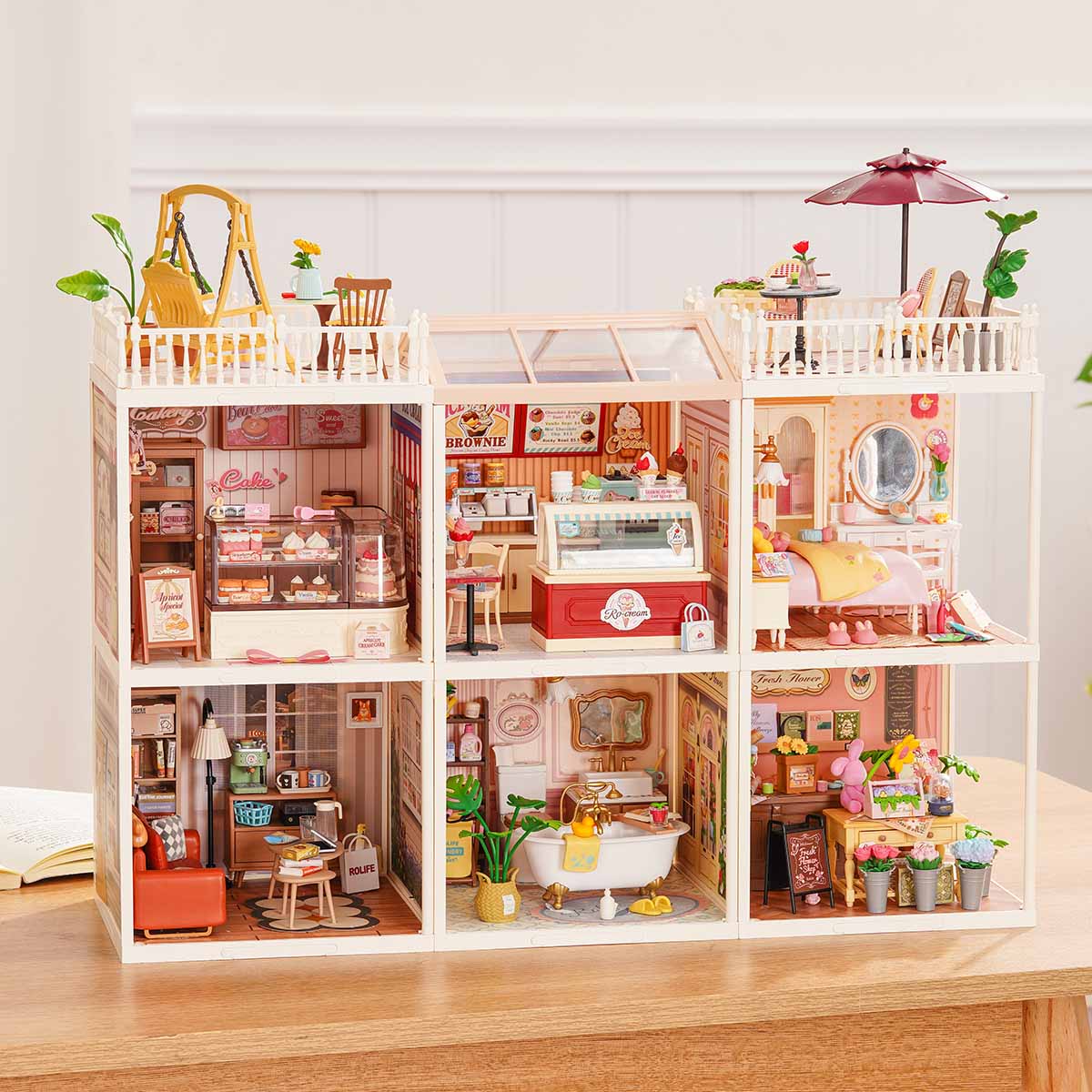 Rolife Super Creator Series 6-in-1 Six Grid horizontal miniature with coffee shop, supermarket, fruit store, bar, bookstore, and afternoon tea rooms in a wide white frame on a table.