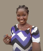 Smiling female blog author portrait wearing a blue, white, and gray chevron top with a gold love necklace against a neutral beige background