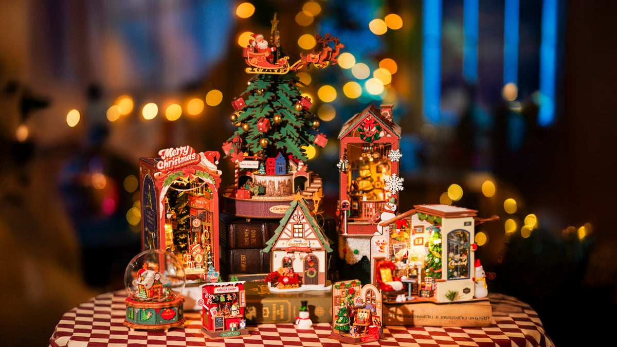 Rolife Christmas collection table display with multiple illuminated book nooks and miniature holiday houses on a checkered cloth with warm bokeh lights.