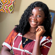 Robotime blog author Ihendeson Ehinomen headshot, smiling woman in a colorful patterned dress with curly hair, warm background with African fabric art