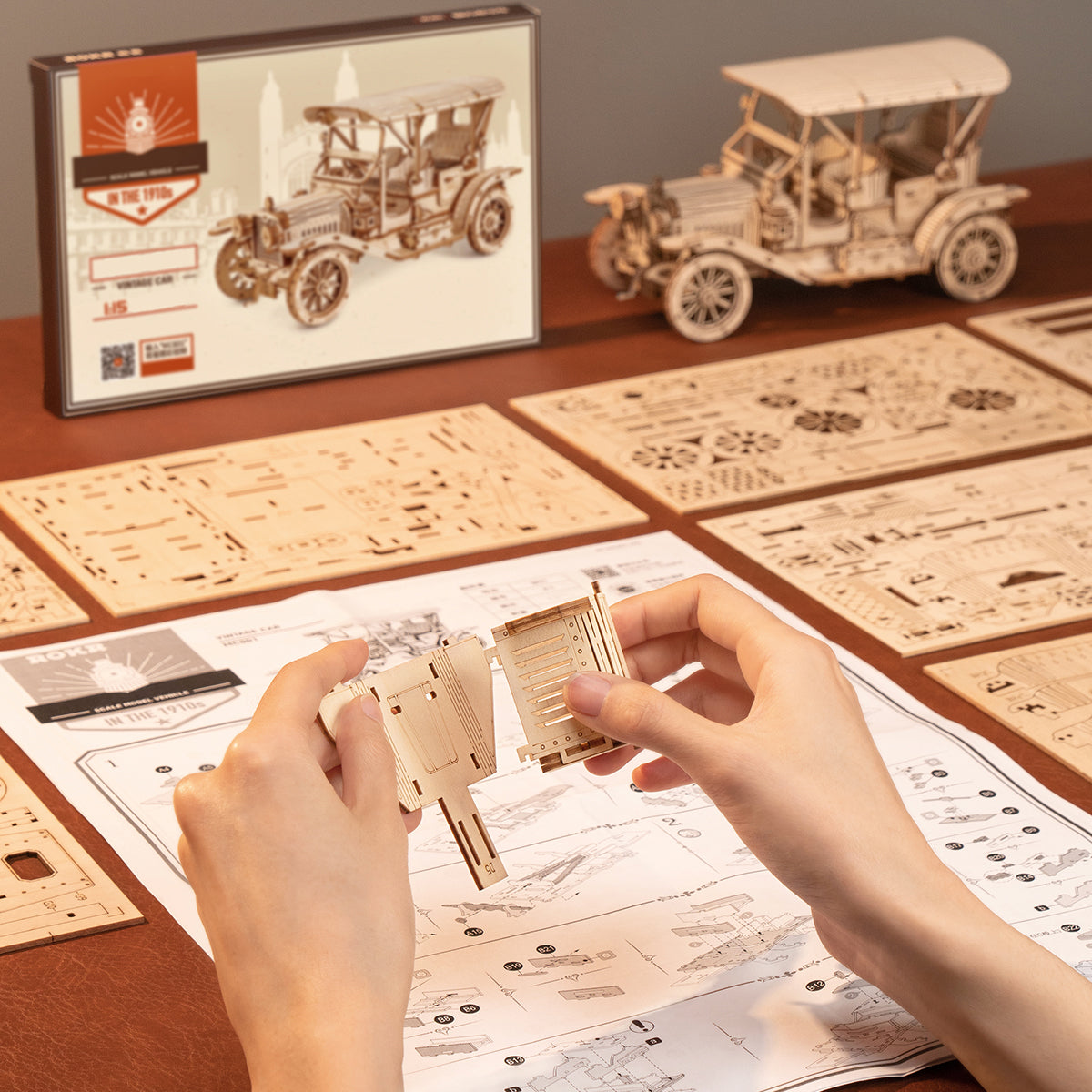 ROKR Vintage Car MC801 assembly scene with hands fitting laser-cut wooden parts, box and finished model visible