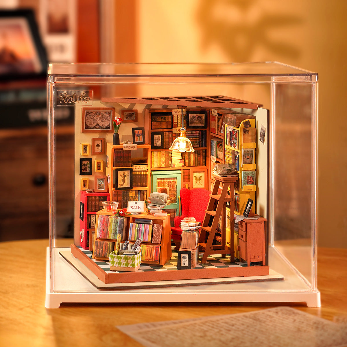 Rolife Sam's Study Library DIY miniature house DG102 inside a clear acrylic display box with warm LED lamp illuminating walls of books and colorful shelves