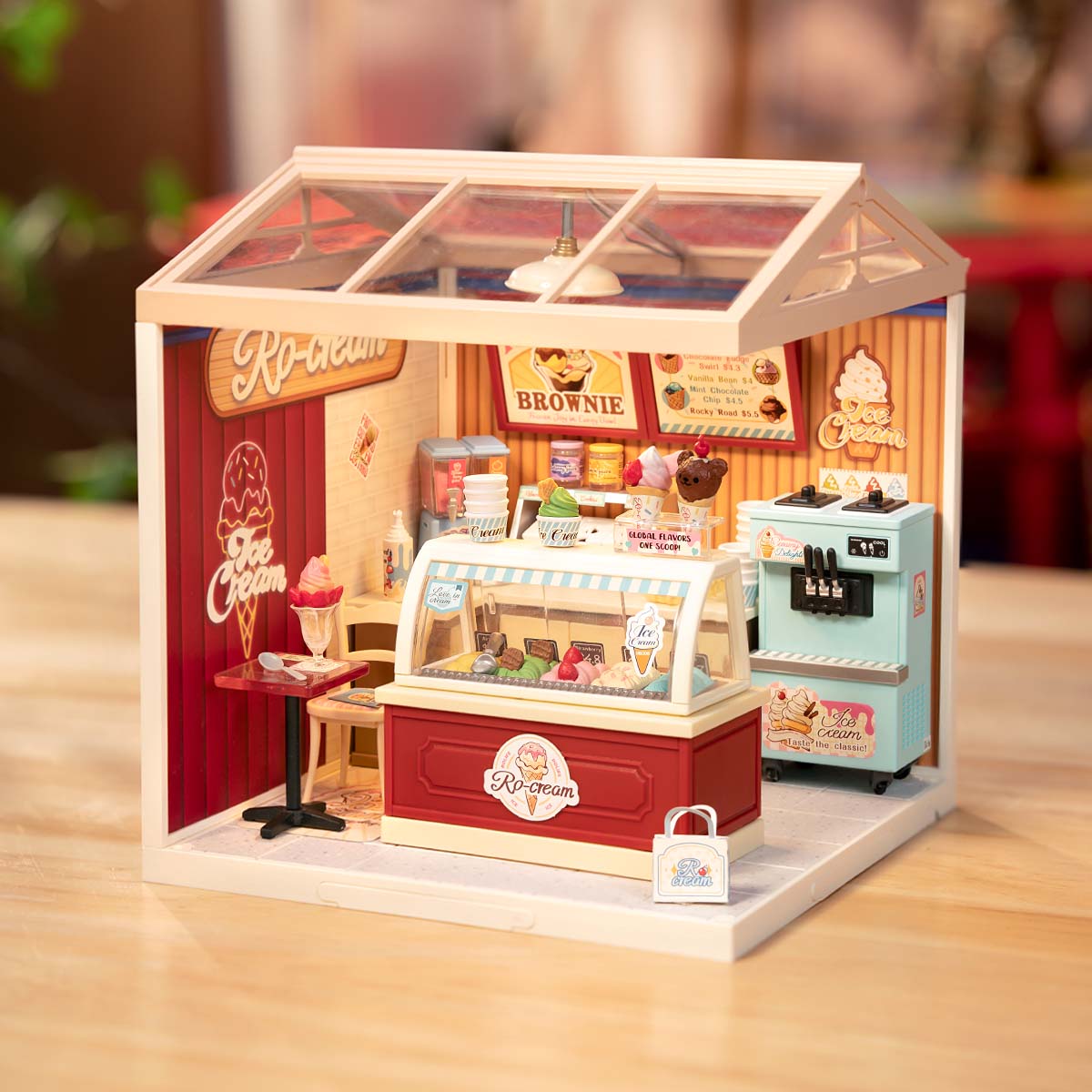 Rolife Flavorful Ice Cream DIY miniature house DW018B lifestyle scene showing the completed red-themed ice cream shop with Ro-cream branding, brownie menu board, and soft warm ambient lighting.