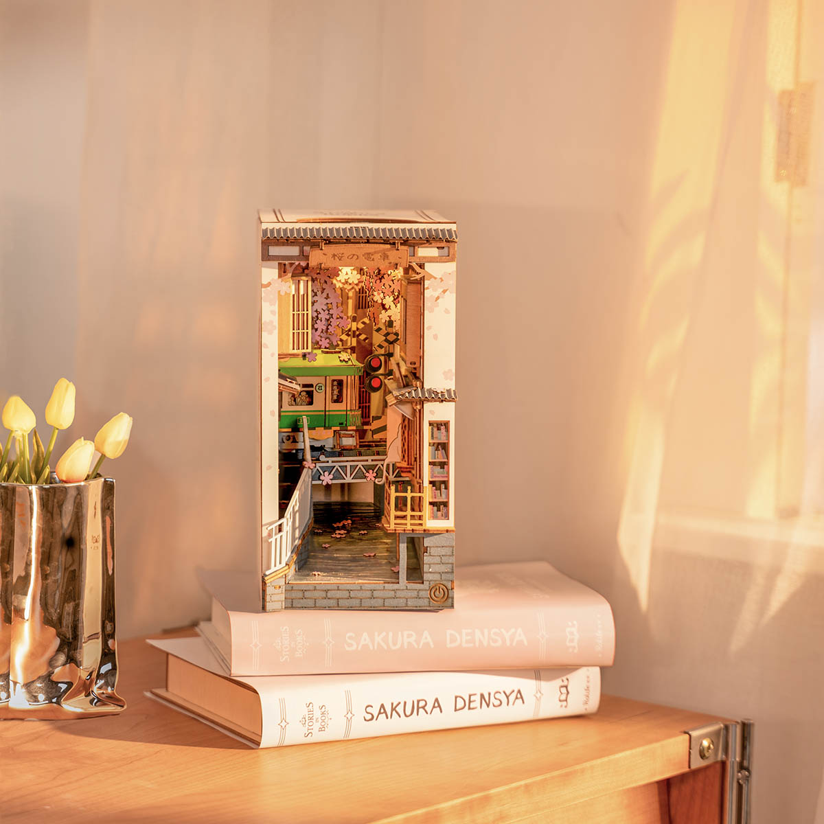 Book nook Rolife Sakura Densya exposé sur des livres à côté de tulipes sous une lumière d'après-midi chaleureuse