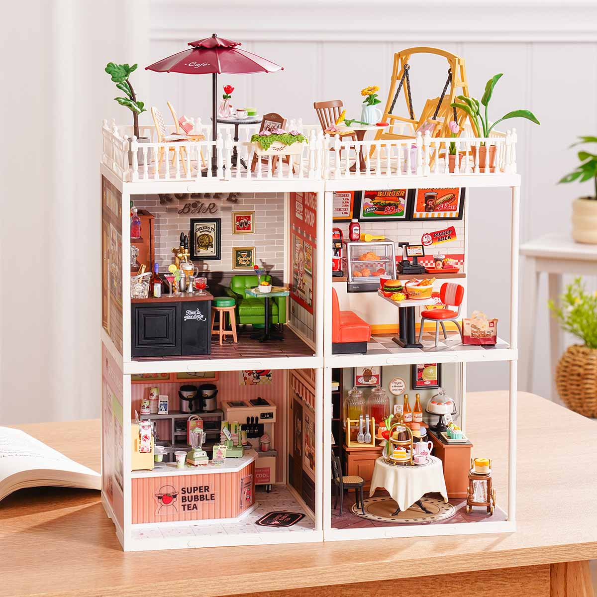 Rolife Super Creator Series 4-in-1 Four Grid miniature showing Rolife Bar, burger shop, afternoon tea, and bubble tea rooms arranged in four grid cells on a wooden table beside a plant.