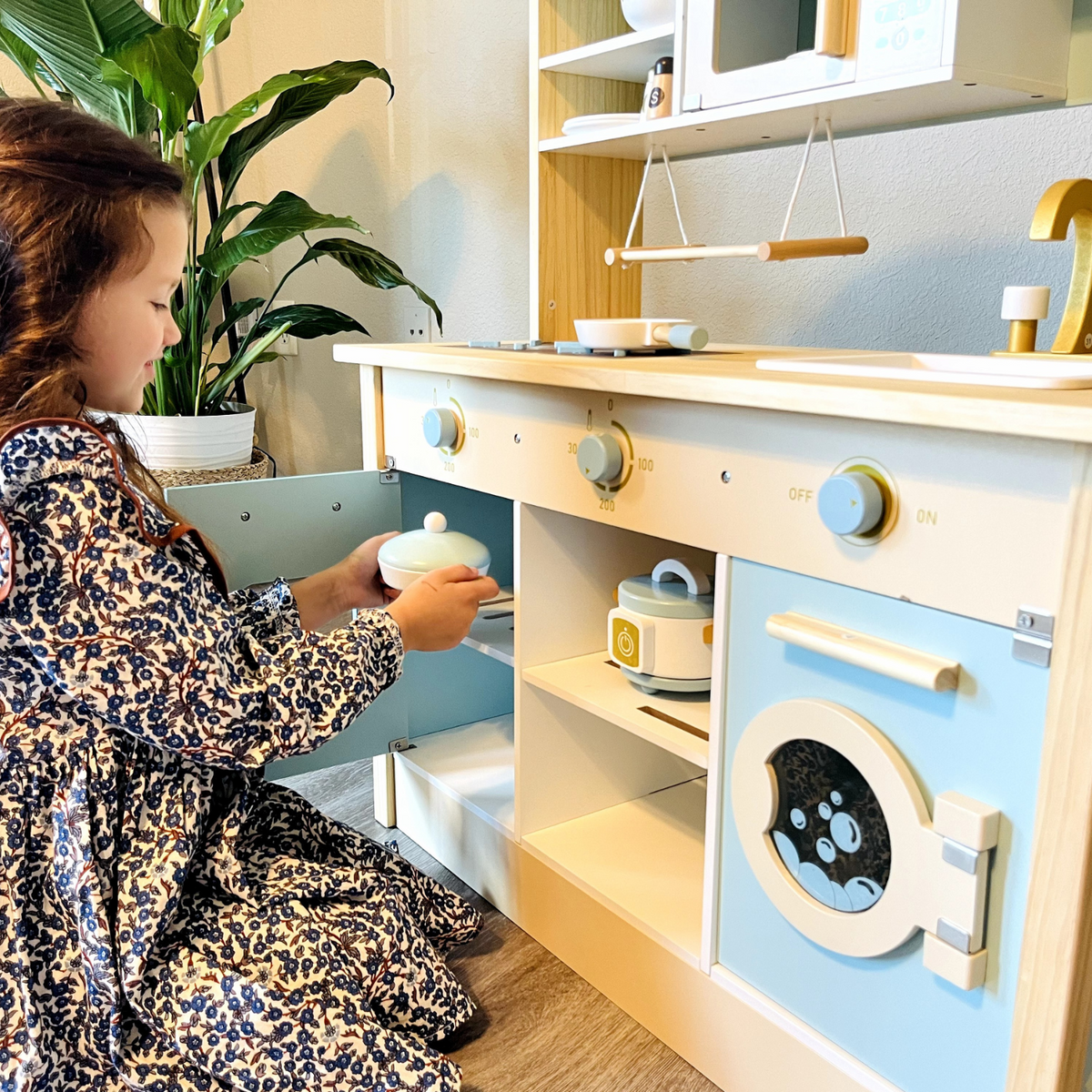 ROBUD WCF14 Montessori play kitchen lifestyle scene with a girl sitting and playing beside the set.