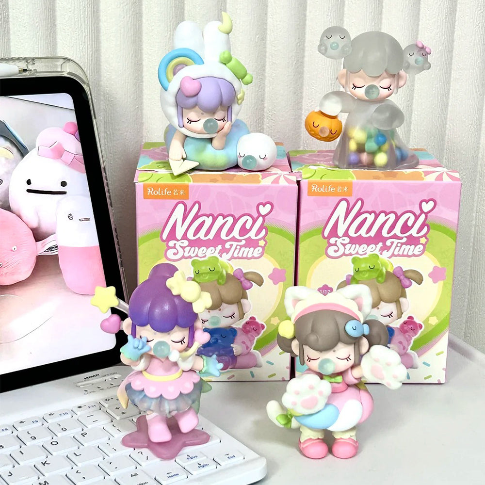 Rolife Nanci Sweet Time surprise figure dolls displayed beside pink branded boxes on a desk with a tablet and soft toys in the background