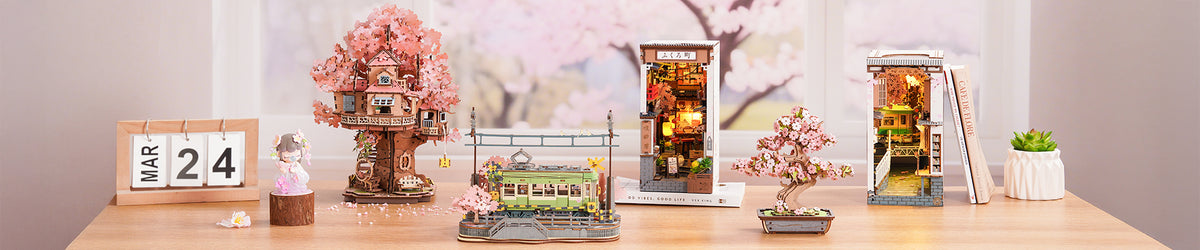 Robotime Sakura collection wide desktop banner showing four Rolife cherry blossom themed miniature kits arranged on a wood desk with a Mar 24 calendar tile and pink blossom window backdrop.